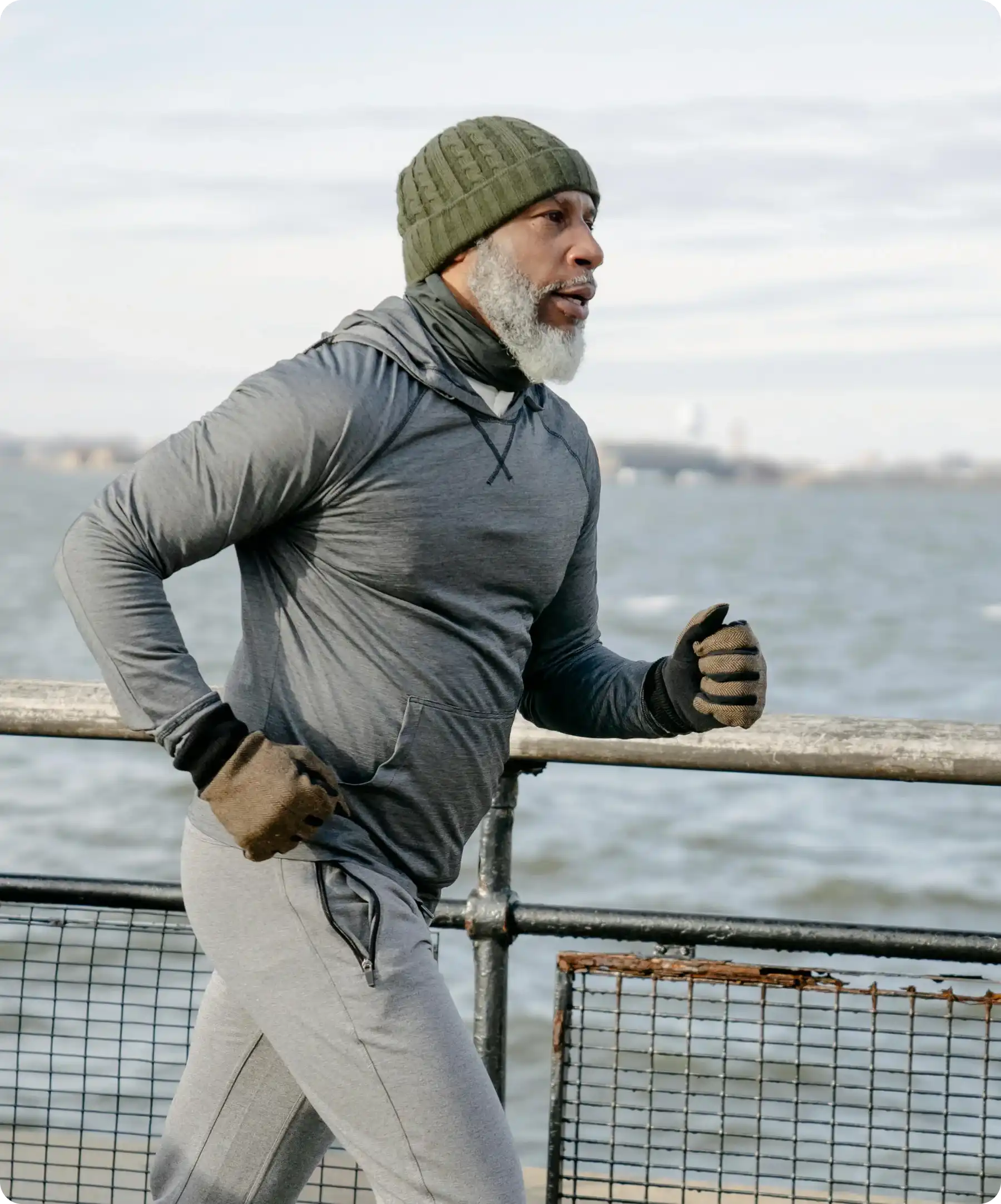Man jogging on a waterfront path wearing winter clothing.